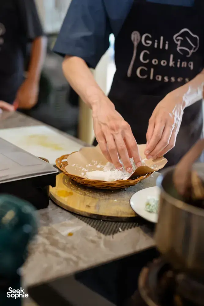 Hands pressing dough in a woven tray at a Gili T cooking class in Lombok, with Gili Cooking Classes aprons