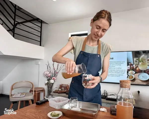 The TCM Chef pouring a crafted TCM mocktail into glasses in a kitchen classroom in Singapore for workshops in Singapore