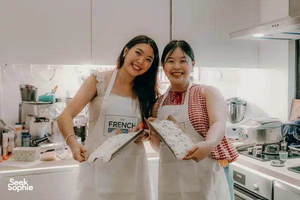 Two participants in aprons holding flour-dusted baguette dough during French bread making with French Cooking Lab workshops in Singapore