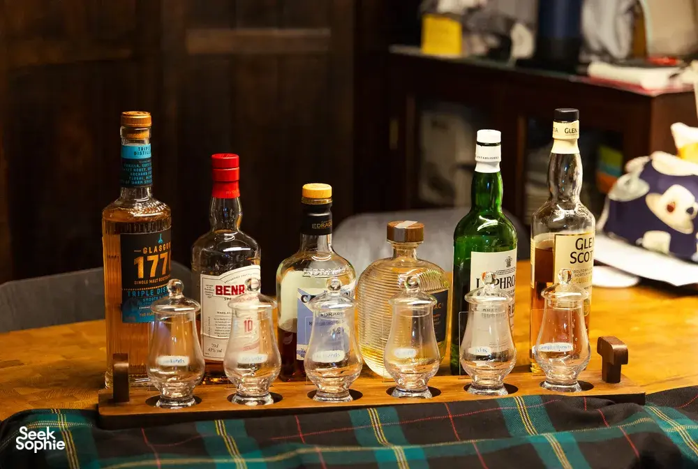 Row of whisky bottles and small tumbler glasses on a tray at a hidden home bar in Katong, Singapore, ready for small-batch tasting