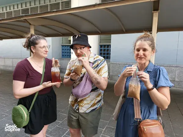 Three walkers holding takeaway drinks and posing outside in Geylang, Singapore on a private night walk — Singapore hidden gems