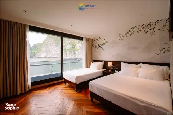 Sunshine Golden Cruises suite cabin with two beds and wide window framing limestone cliffs on a Cat Ba 2D1N cruise
