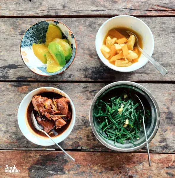 Bowl of fruit, leafy greens and soup plated on a wooden table at Ngapuh Homestead’s regenerative homestead near Kuching