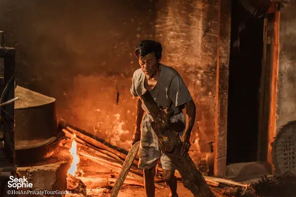 Ha carrying firewood through a lantern-lit doorway in Hoi An, showing everyday trades on an early-morning tour