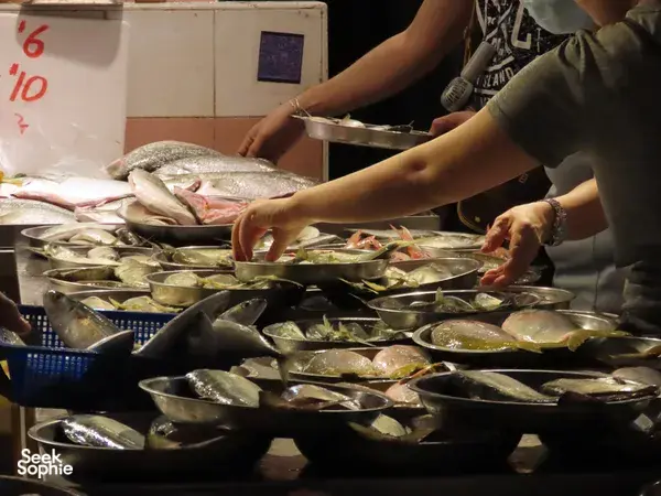 Hands preparing fresh fish on metal trays at a Singapore seafood hawker stall during a Cantonese fish tour experience