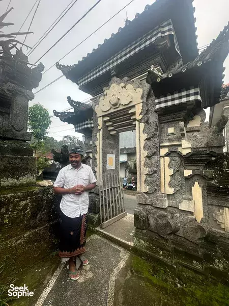 Local guide in a sarong stands at a carved Balinese temple gateway during the Tri Hita Karana philosophy journey in Bali