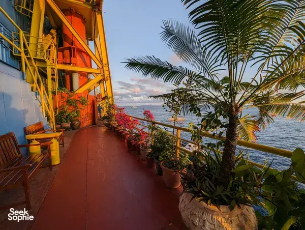 Tiled walkway beside orange rig structures, potted plants and an ocean horizon at sunset during a Seaventures Dive Rig stay