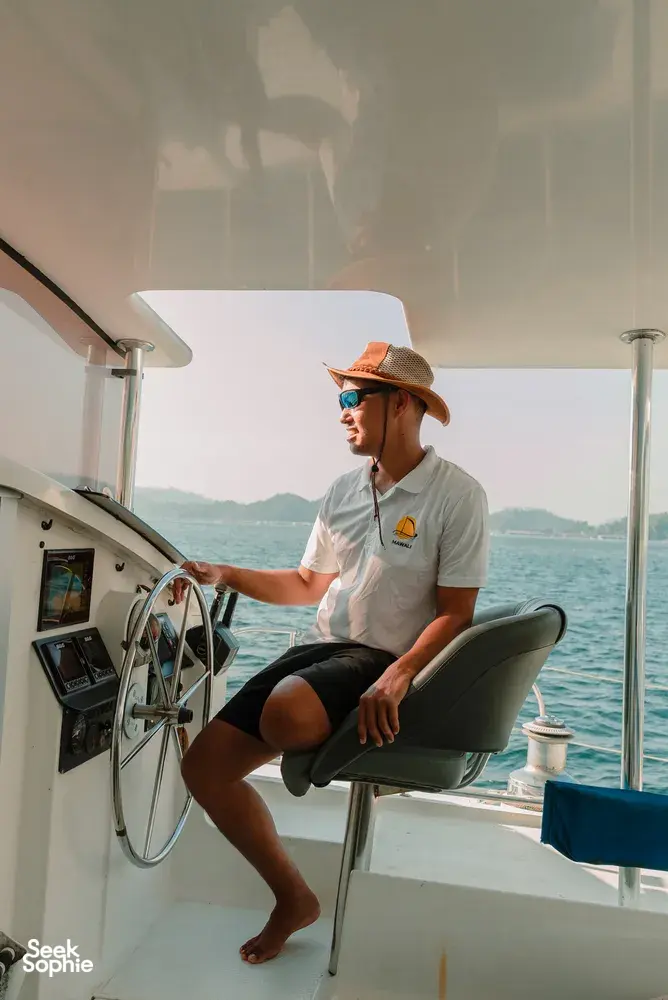 Jerry Reichart of Mawali Sailing steering a catamaran on the sea off Kota Kinabalu, with distant hills in view
