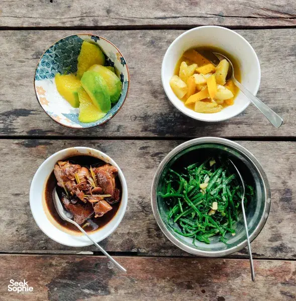 Assorted local dishes on a wooden table in Kuching: cucumber salad, noodle soup, braised meat, and stir-fried greens