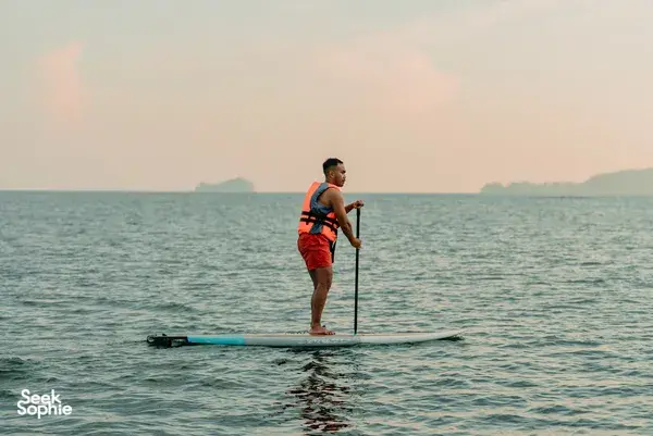 Stand-up paddleboarder on calm sea at sunset with distant islands near Kota Kinabalu
