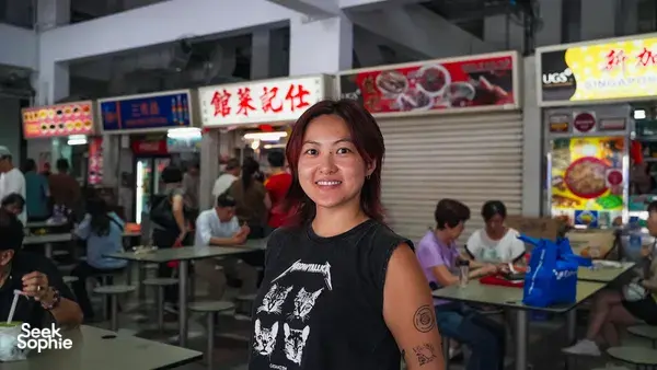 Chef Jenny Dorsey Culinary Consulting smiling by a Singapore hawker centre stall, with diners and signage nearby — Singapore hidden gems
