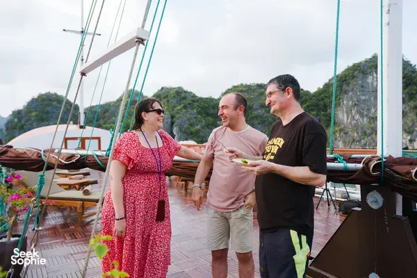Travellers chatting on the deck of a boutique wooden cruise in Cat Ba National Park, with limestone cliffs across the bay