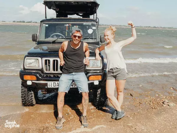 Smiling couple on a 4x4 safari jeep on a sandy riverbank in Udawalawe, ready to explore the national park