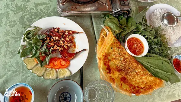 Plates of appetisers with greens and dipping sauces on a table during a meal break on a Mekong Delta tour