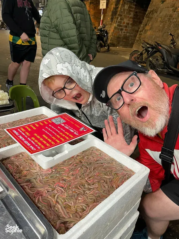 Travellers grinning at a Hanoi street food stall, leaning over an ice tray of ingredients during a guided food adventure