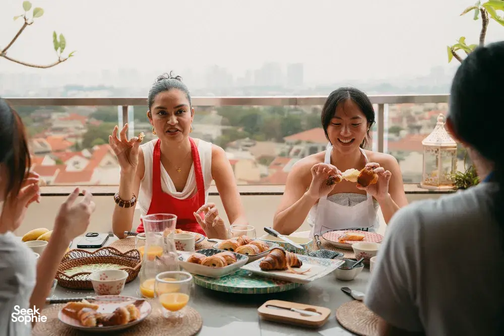 Balcony breakfast in Singapore: people hold freshly baked croissants at a long table with city skyline beyond the railing