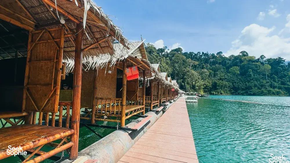 Family-run Khao Sok Riverside Cottages rafthouse walkway over the water, lined with cottages and greenery, in Cheow Lan Lake