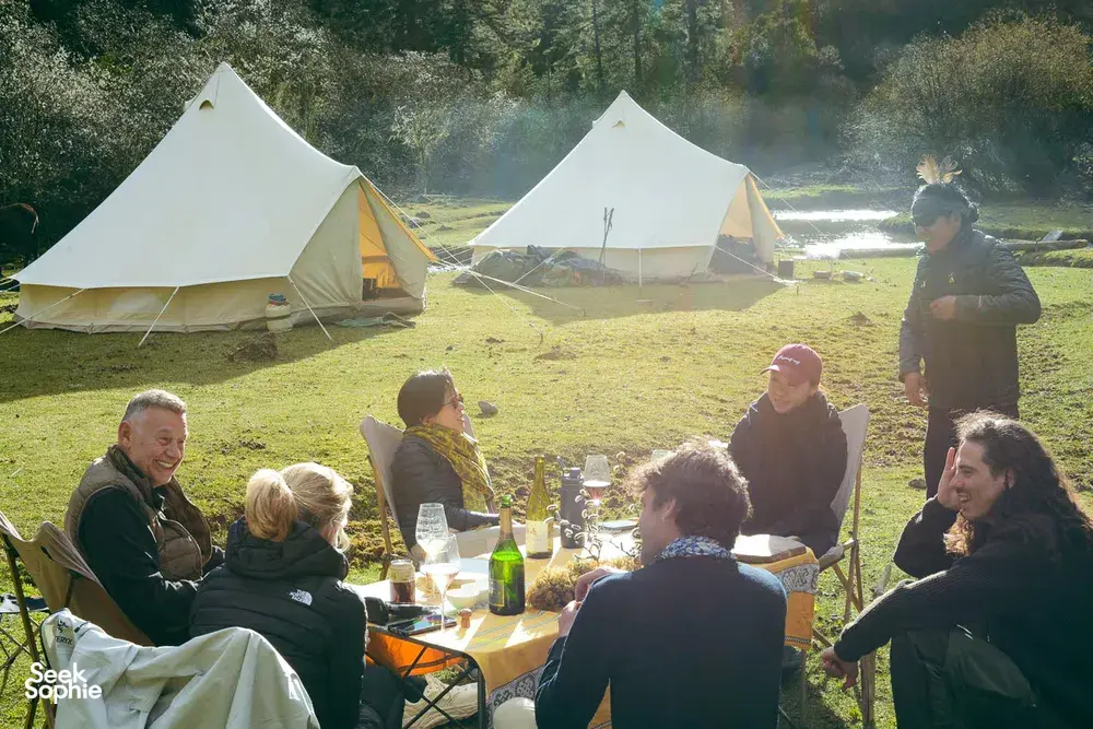 Travellers sharing dinner at a valley camp with white tents and glowing lanterns, part of a caravan trek stay near Shangri-La