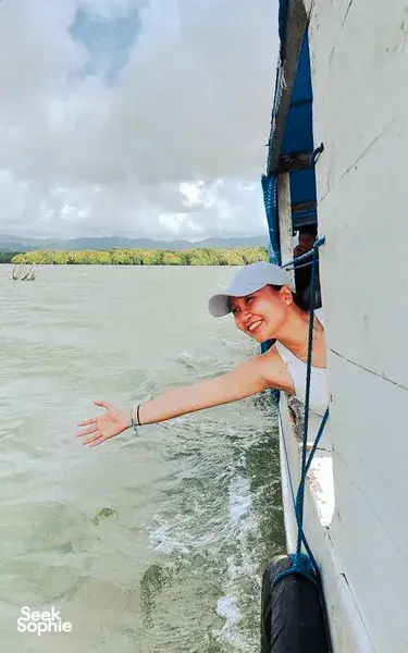 Smiling traveller holding onto a white boat rail as it moves through green seascapes during a hidden mangroves day trip, Labuan Bajo