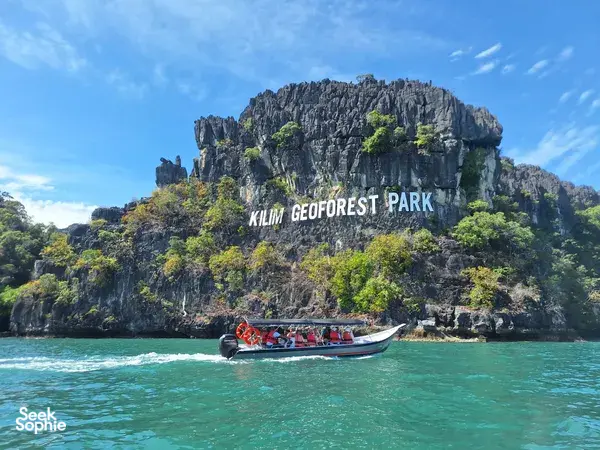 Speedboat with passengers cruising turquoise waters toward the limestone wall of Kilim Geoforest Park, Langkawi with Dev's Adventure Tours