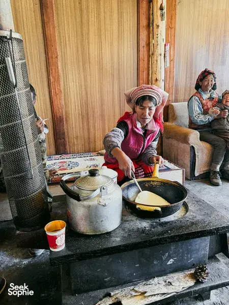 Traditional guesthouse kitchen in Lijiang, with a local cook stirring a pan on the stove during the Yi & Naxi trek stay