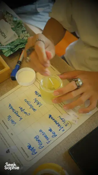 Hands stirring yellow wax in a glass jar over a recipe sheet for scented coco-soy candles, workshops in Singapore