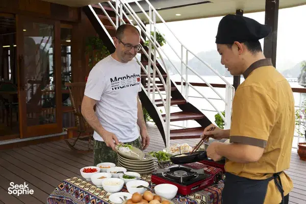 Chef and staff arranging a breakfast buffet on the deck of a Cat Ba boutique cruise, with dishes and bay views