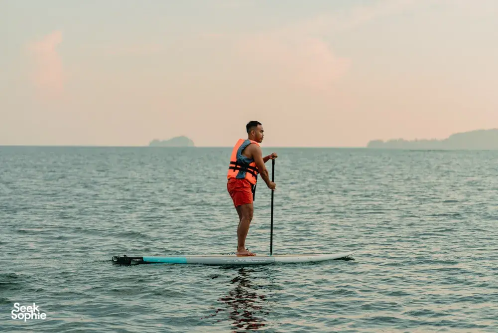 Stand-up paddleboarder on calm sea at sunset with distant islands near Kota Kinabalu