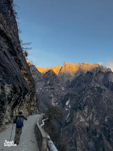 Hiker with trekking poles walking the cliffside switchback path in Tiger Leaping Gorge near Lijiang at dawn on the 2D1N high trail