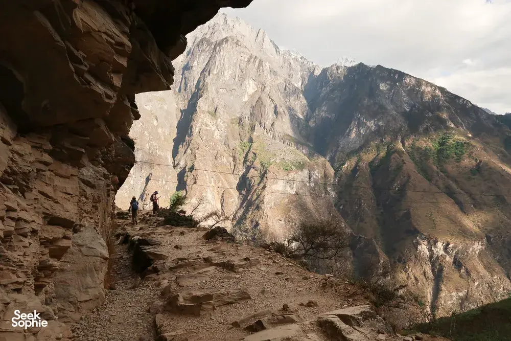 Hikers on the High Trail of Tiger Leaping Gorge in Lijiang, framed by steep rock walls and mountain valley views