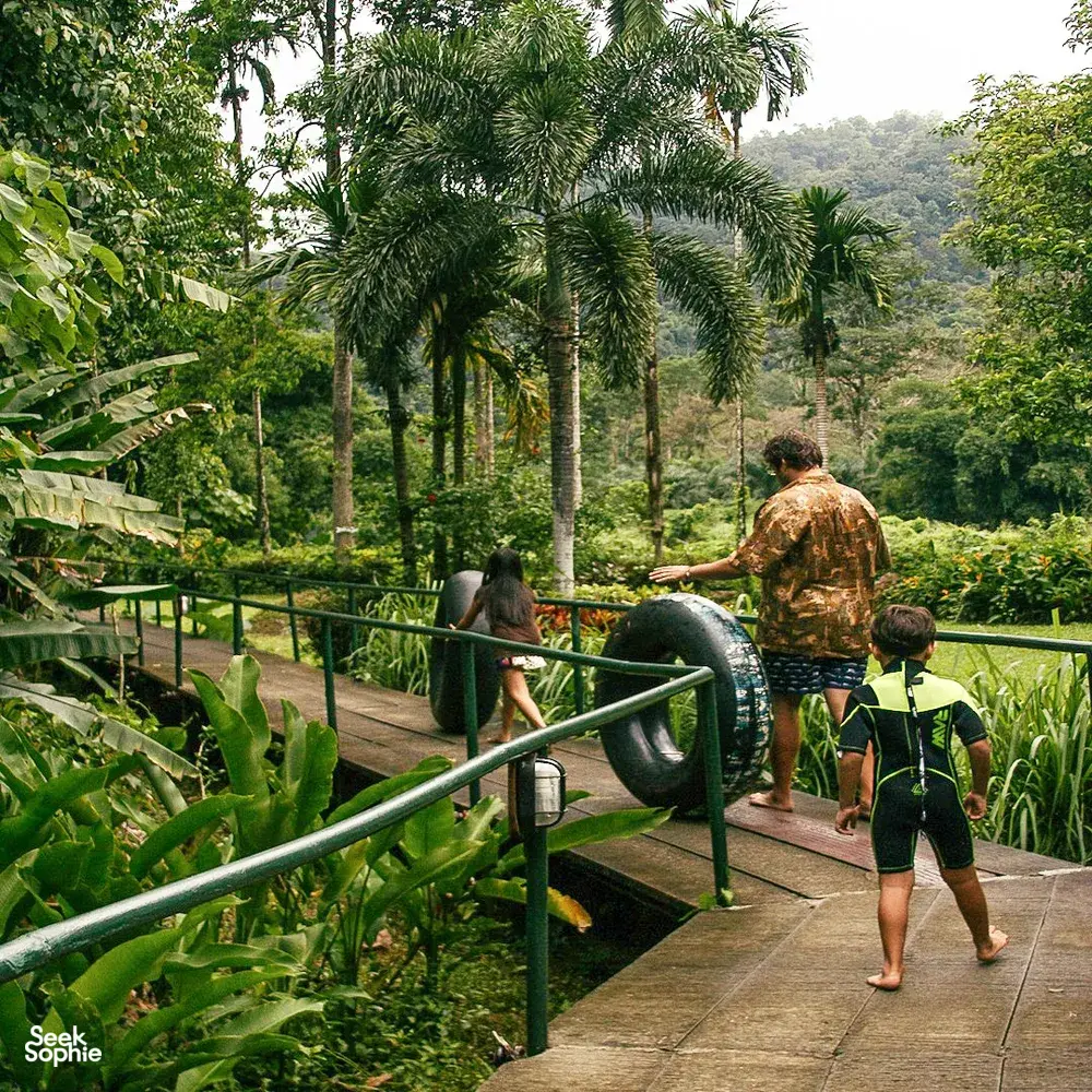 Khao Sok Riverside Cottages deck with a family on a riverside walkway, surrounded by palms near Cheow Lan Lake