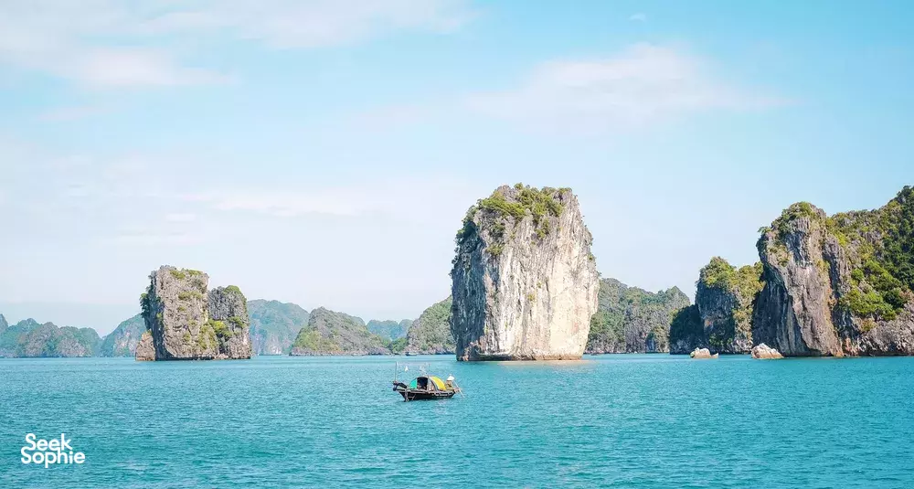 Open-water view of limestone islets with a small boat on Cat Ba Bay, part of a 3D2N Cat Ba cruise
