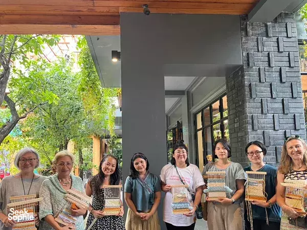 Group of workshop participants holding woven pieces outdoors at Kalm Village in Chiang Mai, celebrating learning traditional Thai weaving