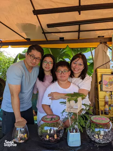 Family group smiling under a garden canopy with several terrariums on the table, celebrating a terrarium workshop in Singapore