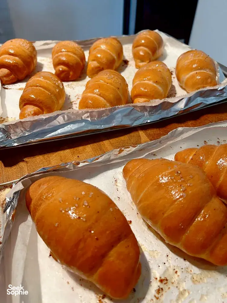 Assorted shio pan buns brushed with glossy glaze on two foil-lined trays, fresh from the oven at a Singapore bake class