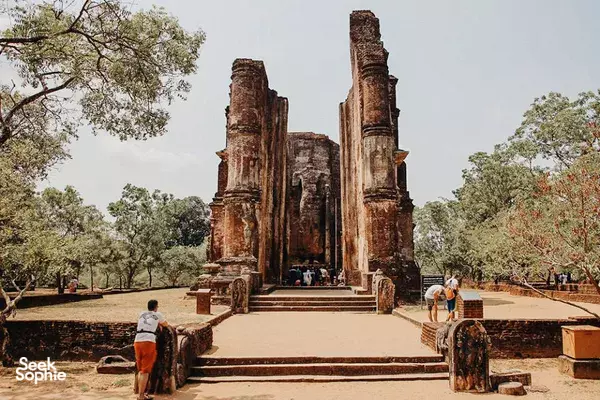 Visitors walking through an open courtyard of tall ruined stone columns, with trees framing the ancient temple site in Polonnaruwa