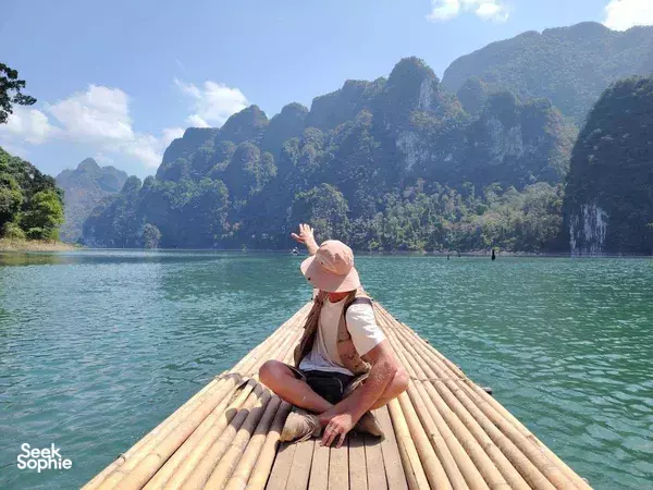 Bamboo raft on a calm lake in Thailand, with a traveller relaxing as limestone cliffs rise in the distance
