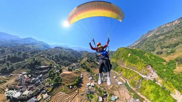 Tandem paraglider soaring above terraced rice fields and mountain valleys with Sapa Paragliding under a bright canopy over Sapa