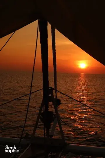 Siluet layar dan tali-temali berlatar matahari terbenam di laut saat berlayar dengan yacht pribadi saat senja dari Kota Kinabalu, Sabah
