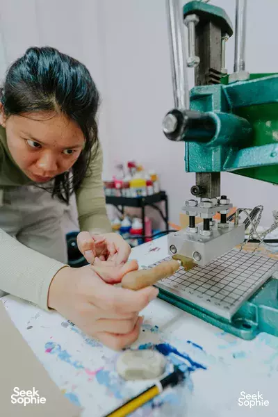 Participant using a green leather-stamping press and tools in a studio, crafting a leather journal cover — workshops in Singapore