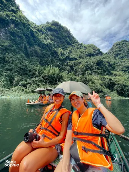 Travellers waving from a small boat with life jackets against towering limestone cliffs in Ninh Binh on a private day tour