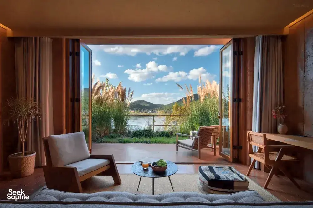 Lounge terbuka di eco retreat Linden Centre di Shaxi, Dali, dengan pintu kaca yang menghadap ke danau berpagar alang-alang