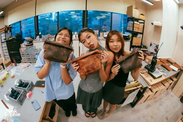 Friends holding handmade leather bags at Crafune leathercraft studio in Singapore—workshops in Singapore