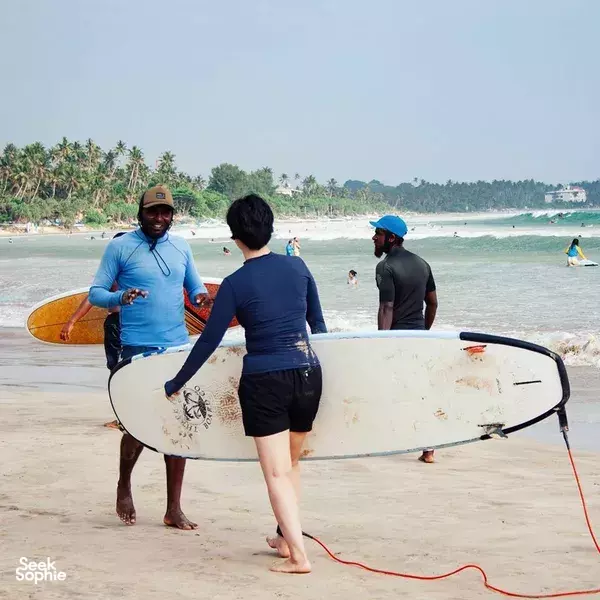 Freedom Surf Sri Lanka coach talking with a small group on Weligama beach, holding a longboard as students get ready