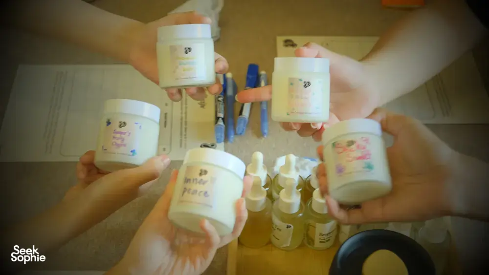 Multiple scented coco-soy candle jars held up at once after making blends at Perfume Play in Singapore candle workshop