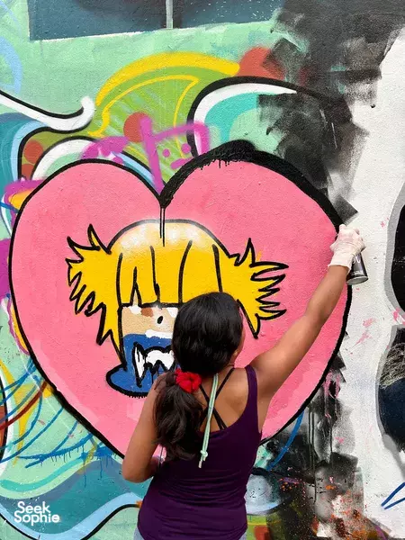 Da Nang graffiti art workshop: participant spraying a heart-shaped mural on a wall while another works alongside with spray cans