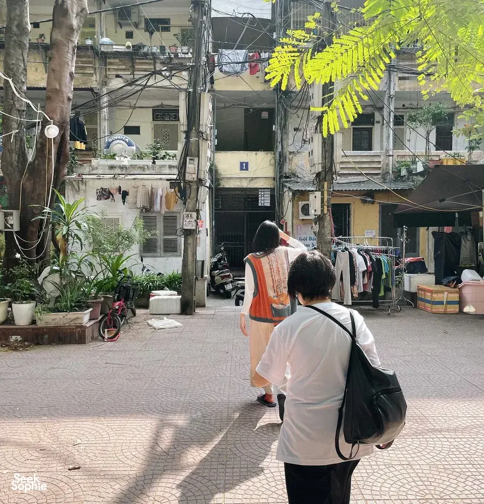 Walkers in matching vests on a quiet laneway in Hanoi, passing potted plants, laundry lines and old apartment blocks.