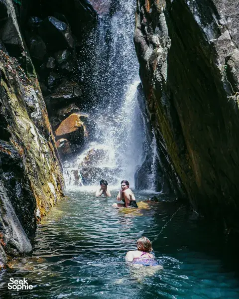 People wading in a narrow gorge pool as water cascades down the rocks on a Hoi An secret waterfall stop