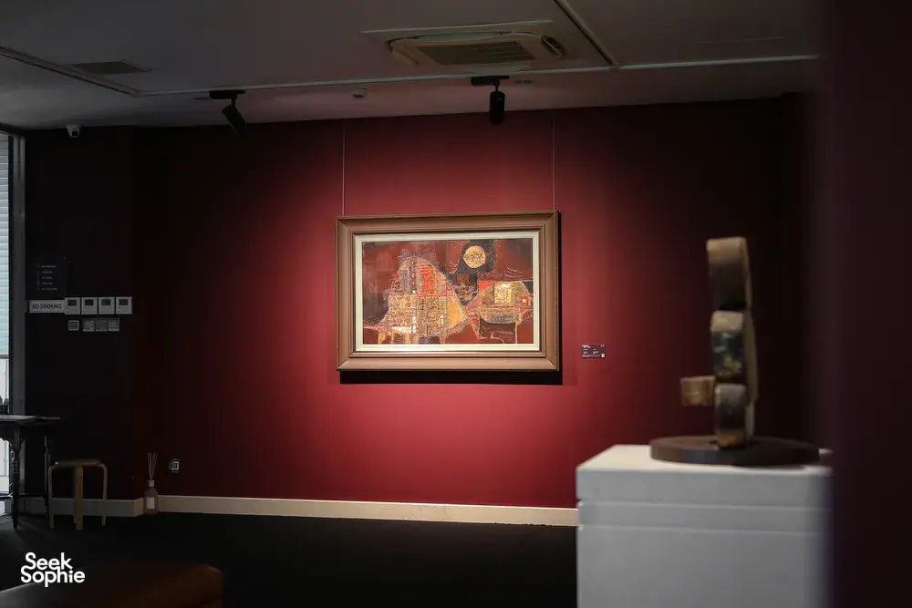 A framed painting on a red gallery wall and a display pedestal inside Quang San Art Museum in Ho Chi Minh City