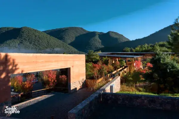 Halaman Linden Centre di eco-retreat Shaxi, Dali, dengan bangunan batu, pepohonan musim gugur, dan pegunungan saat senja